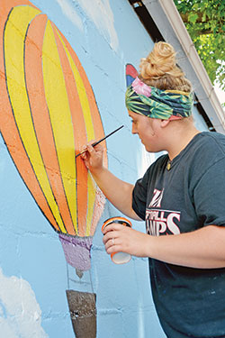 Alex Moehn of Kimberly, Wis., paints a mural for the children’s play area on the St. Elizabeth Catholic Charities campus in New Albany on June 19. (Photo by Natalie Hoefer)