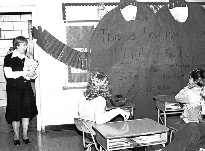In this photo, eighth-grade students at St. Vincent de Paul School in Bedford celebrate Teacher Appreciation Day during Catholic Schools Week in January 1983. Their teacher was Franciscan Sister Joan Luerman. The writing on the giant paper heart reads, “Sister Joan, This is how much we love you,” and is signed by all of the members of the class.