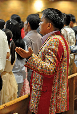 Paul Hnin, a refugee from the Hakha Chin region of Myanmar, wears a suit coat made with traditional Hakha Chin material as he raises his hands in prayer during a Mass celebrated in his native language by Bishop Lucius Hre Kung, visiting from the Hakha Diocese in Myanmar, at St. Barnabas Church in Indianapolis on Aug. 4. (Photo by Natalie Hoefer)