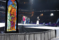 Franciscan Friar of the Renewal Father Agostino Torres and a group of youths lead National Catholic Youth Conference participants in a period of lectio divina (“holy reading”) prayer on Nov. 22 in Lucas Oil Stadium in Indianapolis. An image depicting part of the story from the Gospel of St. Luke about the disciples on the road to Emmaus created by Benedictine Brother Martin Erspamer sits adjacent to the main stage during the prayer session. (Photo by Sean Gallagher)