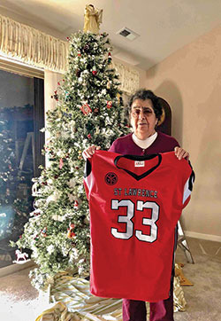 Mary Devine shows the football jersey that she received from the fifth-and-sixth grades’ football team of St. Lawrence Parish in Indianapolis. The team gave her the jersey after the Nov. 20 funeral Mass for her husband, Patrick Devine, who had coached boys at the parish for 40 years. (Submitted photo)