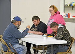 Dee Traub of Our Lady of Perpetual Help Parish in New Albany, standing, shares in conversation as Mark Russell, second from left, and two other guests enjoy a hot meal at the White Flag shelter in New Albany on Feb. 7. (Photo by Natalie Hoefer)