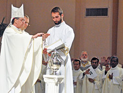 Joined by several priests serving in the archdiocese, Archbishop Charles C. Thompson blesses chrism oil during the annual chrism Mass on April 16, 2019, in SS. Peter and Paul Cathedral in Indianapolis. Assisting in the liturgy are then-transitional Deacon Vincent Gillmore, second from left, and seminarian Justin Horner. (File photo by Sean Gallagher)
