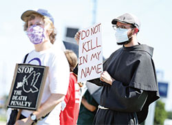 Right, Conventual Franciscan Brother Ian Bremar holds a sign during an anti-death penalty protest in Terre Haute on July 17. (Submitted photo by Scott Langley)