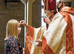 Archbishop Charles C. Thompson places chrism oil on the forehead of Taylor Borden in the sacrament of confirmation during a Nov. 1 Mass at St. Paul Church in Tell City. Taylor is a member of St. Isidore the Farmer Parish in Perry County. (Submitted photo by Danny Bolin)