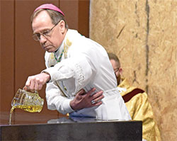 Archbishop Charles C. Thompson pours chrism oil on the altar of St. Michael Church in Greenfield during a Jan. 30 dedication Mass of the recently renovated church. Looking on is Father Douglas Marcotte (partially obscured), pastor of St. Simon the Apostle Parish in Indianapolis who grew up in St. Michael Parish. (Photo by Sean Gallagher)