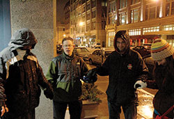 Andrew Costello, second from left, leads a prayer on the night of Feb. 21, 2013, as members of Operation Leftover take to the streets of downtown Indianapolis to provide food, clothing and conversation with people who are homeless. The group of young adult Catholics dedicated to helping the homeless is based at St. John the Evangelist Parish in Indianapolis. Costello prays with a man who is homeless, left, and two other members of the group, Michael Gramke, second from right, and Kellye Cramsey. Costello is stepping aside as coordinator of the ministry to focus on his family.  (File photo by John Shaughnessy)