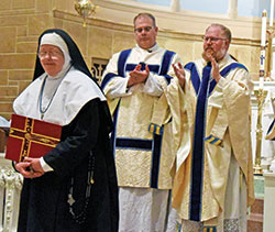 Sister Elizabeth Mary of the Visitation, previously Ellen Carney, receives applause after professing vows as a hermitess of the Archdiocese of Indianapolis during an April 26 Mass at Our Lady of the Most Holy Rosary Church in Indianapolis. Joining in the applause behind Sister Elizabeth Mary are Father C. Ryan McCarthy, left, and Father Joseph Newton. (Photo by Sean Gallagher)