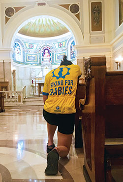 During a stop amid the national ride for Biking for Babies, Emily Mastronicola kneels in prayer at the Blessed Sacrament Chapel of SS. Peter and Paul Cathedral in Indianapolis on July 13. (Submitted photo)