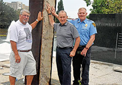 Charles Glesing, left, Tim Baughman and Dave Cook pose on Aug. 25 at the Indiana 9/11 Memorial in Indianapolis. All three were members of Indiana Task Force 1, an elite urban search and rescue team deployed to ground zero in New York City less than a day after terrorist attacks destroyed the twin towers of the World Trade Center on Sept. 11, 2001. They are touching a steel beam taken from the rubble of ground zero. (Photo by Sean Gallagher)