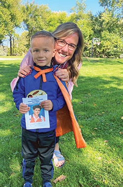 Helen Stephon enjoys a loving moment with her super-hero, cape-wearing grandson, Theo Quillen, who holds a copy of a book about Blessed Carlo Acutis. Stephon, her extended family and others have drawn closer to God through the connection they see between Theo and Blessed Carlo. (Submitted photo)