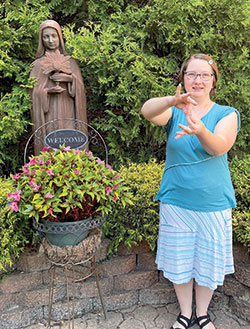 Hannah Houser, a postulant with the Franciscan Sisters in Oldenburg, uses American Sign Language (ASL) by a statue of St. Clare of Assisi on the campus of the sisters’ motherhouse. Although not hearing impaired, Hannah has learned ASL because a disability she has called apraxia can make it difficult for her to speak. (Photo by Sara Geer)