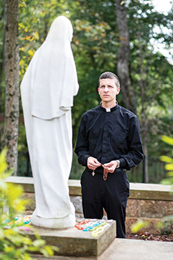 Holding a rosary, seminarian Jack Wright stands before a statue of Mary at the Shrine of Our Lady of Monte Cassino in St. Meinrad. A member of St. Elizabeth Ann Seton Parish in Richmond, Wright credits Mary with guiding him to his priestly vocation. (Photo courtesy of Saint Meinrad Archabbey)