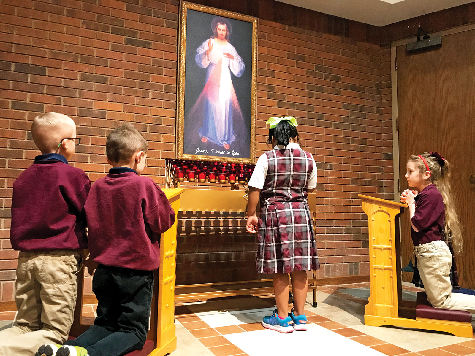 Rebecca Tling, center, lights a candle in the Divine Mercy shrine in St. Barnabas Church in Indianapolis. Praying in the shrine are Harrison Fey, left, Anthony Lewis, Addie Sheehan and Nora Taylor (obscured). The children are first-grade students at St. Barnabas School. (Submitted photo by Joe Sheehan)