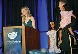 Lauren Niehoff shares the story of her and her husband Brian’s journey of adopting Roslyn, center, while Brian holds their second adopted daughter, Ainsley, during the St. Elizabeth Catholic Charities fundraiser gala at Galt House Hotel in Louisville on April 21. (Photo by Natalie Hoefer)