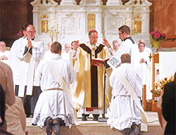 Archbishop Charles C. Thompson prays a prayer of consecration over transitional Deacons Michael Clawson, left, and Matthew Perronie during a June 4 Mass at SS. Peter and Paul Cathedral in Indianapolis in which the deacons were ordained priests. Seminarian Liam Hosty, right, assists during the liturgy. (Photo by Sean Gallagher)