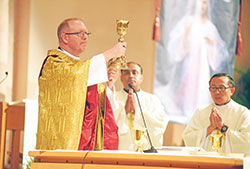 Father Patrick Beidelman elevates the Eucharist during a June 19 Mass at SS. Peter and Paul Cathedral in Indianapolis to start the National Eucharistic Revival in the archdiocese. Concelebrating the Mass are Fathers Jude Meril Sahayam, center, and Minh Quang Duong. (Photo by Sean Gallagher)