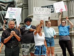 Pro-life youths and young adults stand behind Father Rick Nagel as he offers a prayer of thanksgiving for the Supreme Court’s Dobbs decision during a June 25 prayer gathering on the grounds of the Indiana Statehouse in Indianapolis. A small group of pro-choice protestors shouted as Father Nagel offered his comments and a blessing to both the protestors and the 200 pro-life supporters at the gathering. (Photo by John Shaughnessy)