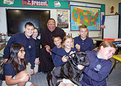 With his dog Guinness surrounded by smiling school children, Father Douglas Hunter doesn’t mind being in the background when he makes a visit to a fifth-grade classroom at St. Roch School in Indianapolis. (Photo by John Shaughnessy)