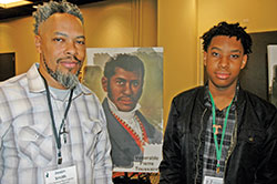 Seeking to grow in their faith and their relationship, Jason Smith and his 15-year-old son Trenton shared time together at the National Black Catholic Men’s Conference in Indianapolis on Oct. 13-16. They posed for a photo by an image of Venerable Pierre Toussaint, a former slave who went on to serve the Church and the poor and who is now up for sainthood. (Photo by John Shaughnessy)