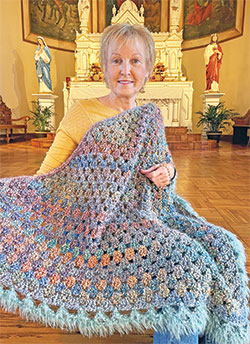 Wrapped in the prayer blanket that she was given after her first cancer diagnosis, Kim Zimmerman has been coordinating the All Saints Parish Ladies Sodality Prayer Shawl Ministry for the past eight years, a ministry that has created 854—and counting—prayer shawls for people facing a crisis in their lives. (Submitted photo)