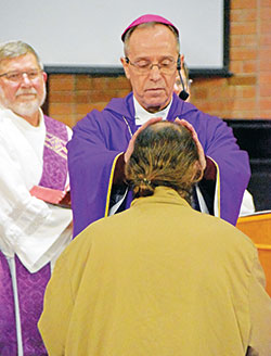 Archbishop Charles C. Thompson, principal celebrant of a Mass celebrated at the Plainfield Correctional Facility in Plainfield on March 26, offers a blessing to a man soon to be released from the facility. Deacon Martin “Neil” May stands at left. (Photo by Natalie Hoefer)