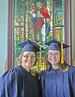 Michelle Williams, left, and Rheann Kelly pose for a photo in front of a stained-glass window in the chapel of the Indiana Women’s Prison in Indianapolis on Aug. 7 after receiving their college diplomas from Marian University in Indianapolis.  (Photo by John Shaughnessy)