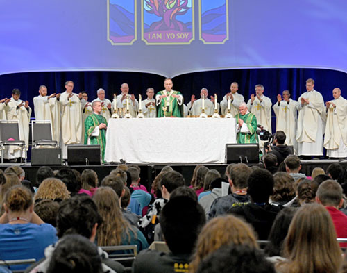 Aaron Bauman, a senior in the San Damiano Scholars program at Marian University in Indianapolis, shows the giant, plastic building block that features an intriguing question for youths at the interactive exhibit hall of the National Catholic Youth Conference in Indianapolis on Nov. 20. (Photo by John Shaughnessy)