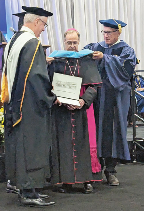 Chemistry assistant professor Dr. Patrick McVey, second from left (obscured), and Toby McClamrock, chair of the board of trustees of Marian University, place a hood over Archbishop Charles C. Thompson during a May 2 commencement ceremony at the school. Looking on is Marian president Daniel Elsener. (Photo by Sean Gallagher)