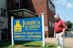 Deacon Richard Grannan stands next to newly-painted sign announcing the new home of Joshua Academy at facilities of St. Joseph Church, Evansville. School began Aug. 3. (Message photo by Paul R. Leingang)