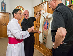 Following the Mass with the Burmese community Bishop Kevin C. Rhoades, center, and Msgr. Robert Schulte, right, admire a chasuble that Archbishop Charles Bo, left, from Rangoon, Burma, gifted to Bishop Rhoades.