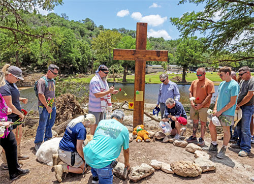 People pray after placing a cross by the Guadalupe River, across from Camp Mystic, following deadly flooding, in Hunt, Texas, July 10, 2025. (OSV News photo/Umit Bektas, Reuters)